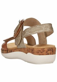 Sandales marron et or avec un dessus texturé, semelle intermédiaire style liège et semelle en caoutchouc blanc. Présente une sangle ajustable et un accent décoratif rond.