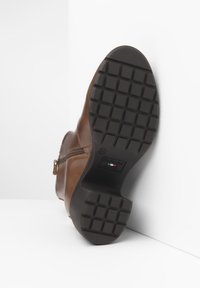 Stivale alla caviglia in pelle marrone con suola in gomma nera testurizzata, dotato di cerniera laterale e di un logo discreto sulla suola.