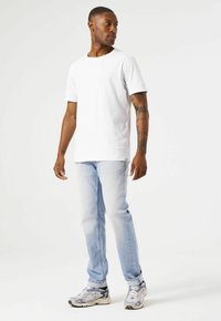 Camiseta blanca de algodón con cuello redondo, combinada con jeans de mezclilla azul claro. El calzado presenta detalles en gris y negro con un diseño de cordones.