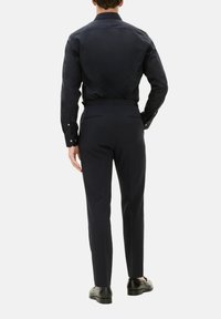 Camicia formale blu scuro con maniche lunghe e polsini con bottone, abbinata a pantaloni su misura coordinati. Tessuto liscio, design aderente, con dettagli minimi.