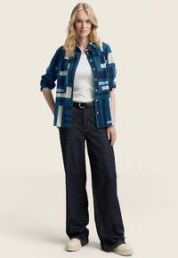 Blauw-wit geruit overhemd met knopen en lange mouwen, gecombineerd met donker wijde jeans en lichtgekleurde schoenen.