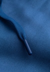 Tissu bleu avec une surface texturée présentant un cordon de serrage tissé. Le cordon de serrage a une pointe lisse et arrondie.