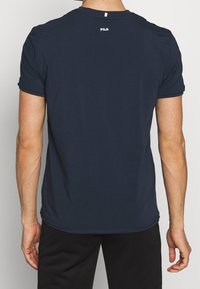 Granatowa bawełniana koszulka z okrągłym dekoltem, krótkimi rękawami i logo na górnej części pleców. Gładka tekstura i standardowy krój.