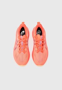 Zapatillas deportivas de color naranja brillante con parte superior de malla, tejido texturizado, acentos morados contrastantes y una lengüeta para tirar en el talón.