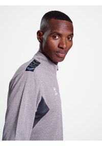 Grijze sportieve kwart-rits shirt met een gestructureerde stof, zwarte accenten op de schouders en een logo op de borst. Glad afwerking, slim fit ontwerp.