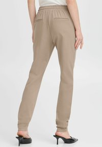 Beige, stretchiga byxor med smal passform, elastisk midja och två bakfickor. Slät textur, i kombination med svarta högklackade skor.