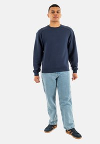 Felpa blu navy con collo a giro, polsini e orlo a costine. Abbinata a jeans azzurri e sneakers nere con accenti beige.