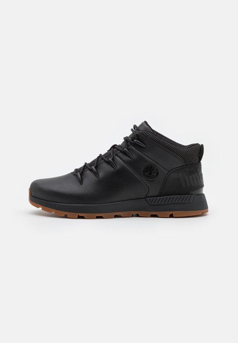 Botte mi-haute en cuir noir avec semelle en caoutchouc marron, fermeture à lacets sur le devant, col de cheville rembourré et logo de la marque embossé sur le côté et le talon.