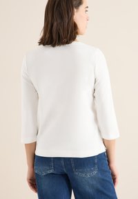 Vit topp med trekvart ärm i ett mjukt material, kombinerad med blå denimjeans, vilket framhäver en enkel och ren design.