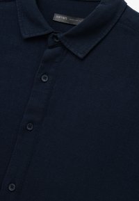 Mørk navy polo t-shirt lavet af struktureret stof. Har en klassisk krave, fem sorte knapper og et mærke, der siger "Koton Casual Regular Fit."