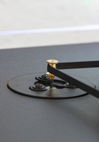 Black metal surface with a brass rod and lever mechanism, surrounded by circular black plastic mounts and visible screws.