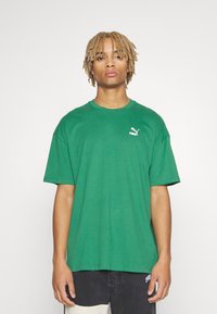 Grøn bomulds T-shirt med korte ærmer, rund halsudskæring og et lille hvidt Puma-logo på venstre bryst. Glat tekstur, afslappet pasform.