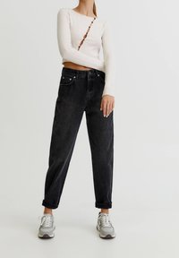 Top de manga larga de canalé beige claro con detalles de botones; jeans de mezclilla negros de cintura alta; zapatillas grises con cordones y acentos blancos.