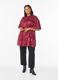 Bordowa tunika w kwiatowy wzór z krótkimi rękawami, zapinana na guziki z przodu, o luźnym kroju. Połączona z czarnymi spodniami o prostych nogawkach i botkami na obcasie.