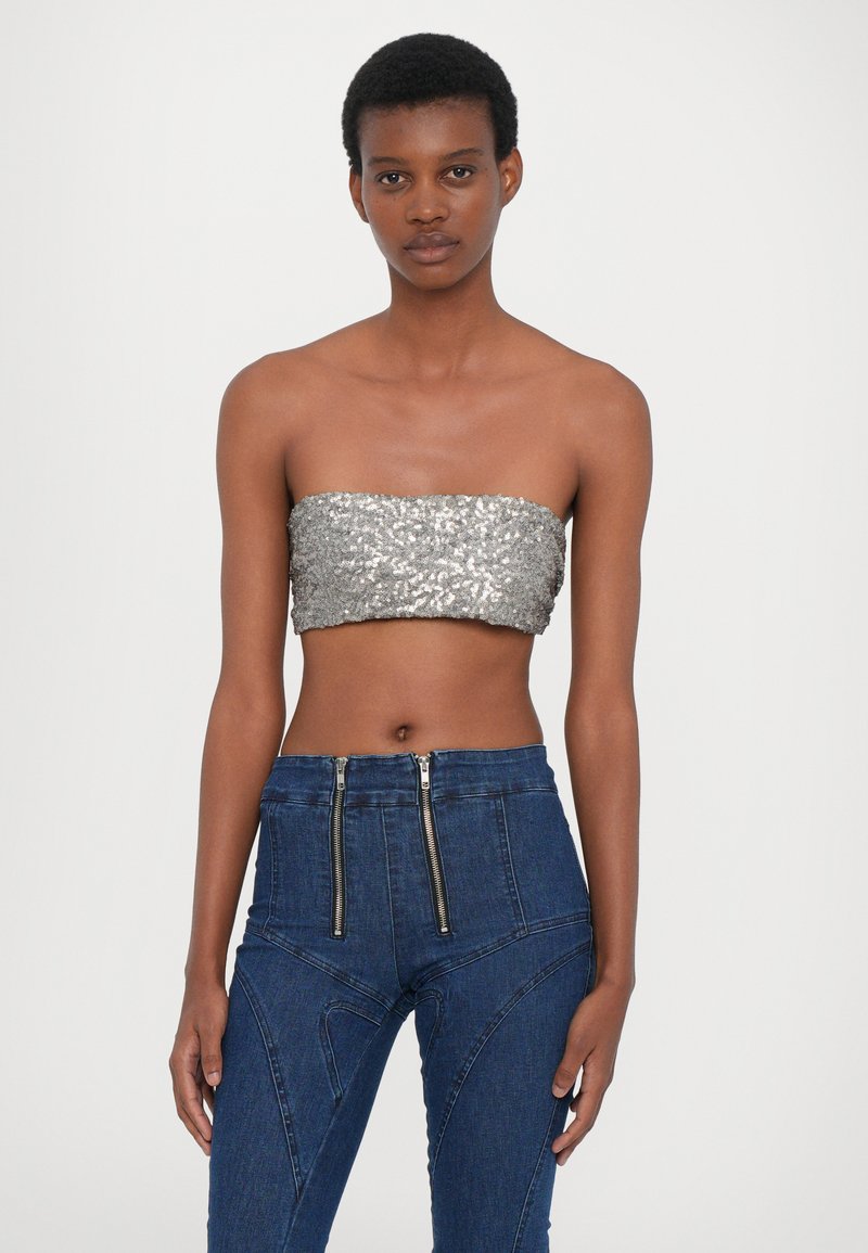 Metallisk silverfärgad paljettklänning utan axelband som är ihopkopplad med höga, mörka denimbyxor med dubbla dragkedjor och strukturerade detaljer.