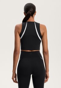 Črni športni crop top z dirkaškim hrbtnim dizajnom, ki ima bele akcentne obrobe ob ramenih. Gladek, raztegljiv material za udobje.