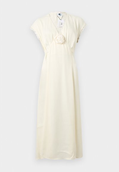 Robe longue de couleur crème avec manches courtes, encolure en V, bordure en dentelle et détail de fleur en tissu à la taille, présentée sur un fond uni.