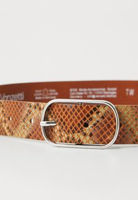 Brun læderbælte med orange og mørkebrune diamantmønstre og sølvfarget oval spænde på hvid baggrund.