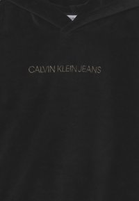 Schwarzer Cord-Hoodie mit V-Ausschnitt und gesticktem "CALVIN KLEIN JEANS"-Logo in Gold. Weicher Stoff mit gerippten Akzenten.