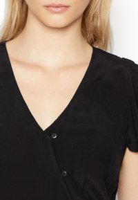 Vestido preto com decote em V e mangas curtas, apresentando dois botões pretos no peito e um tecido suave e texturizado.