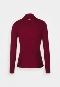 Burgunderfärgad ribbad stickad tröja med långa ärmar, i en smal passform och med peplumstil i midjan. Baksidan har en subtil krage och etikettdetalj.
