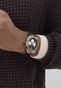 Bruine metalen horloge met een blauwe wijzerplaat, witte subwijzers en gouden accenten. Heeft een gestructureerde band en een genoteerde bezelontwerp.