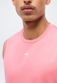 Κοντινό πλάνο ατόμου που φοράει ροζ μπλουζάκι χωρίς μανίκια με μικρό λευκό λογότυπο στο κέντρο του στήθους.