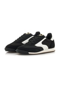 Zapatillas en blanco y negro que combinan ante y materiales sintéticos. Diseño de caña baja, tela texturizada y suela de goma con una raya en contraste.