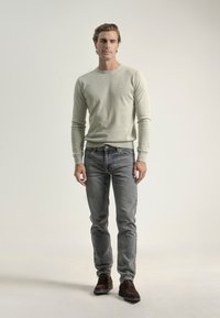 Suéter gris claro hecho de material de punto fino, combinado con jeans azules ajustados y zapatos marrón oscuro. Diseño sencillo, sin patrones visibles.