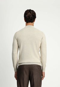 Jasno beżowy sweter z okrągłym dekoltem, prążkowanymi mankietami i dolnym obszyciem. Tkanina ma teksturowany wygląd i dopasowany krój. Nosi się go z brązowymi spodniami.