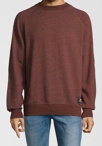 Sudadera de cuello redondo en color burdeos con un tejido texturizado. Presenta mangas raglán y un cuello acanalado. Etiqueta de logo pequeña en el dobladillo inferior.