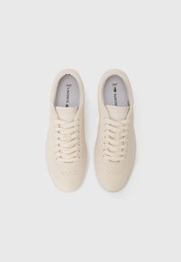 Lacoste-sneakers i lys beige lær, med en glat overflade, hvide snørebånd, perforerede detaljer og et enkelt design.