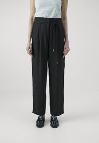 Zwarte, losse linnen broeken met een strik taille en zijzakken. Gecombineerd met zwarte schoenen met ronde uitsparingen en metalen accenten.