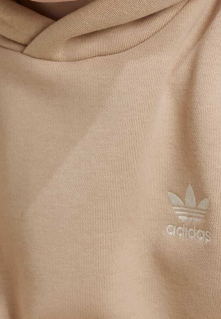 Beige bomullshuvtröja med en mjuk textur, med en tonad broderad Adidas-logotyp på bröstet och en dragsko-hette.