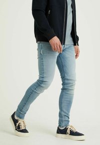 Jeans ajustados de denim azul claro, con un desgaste mínimo, combinados con zapatillas navy que tienen cordones crema y una suela blanca.