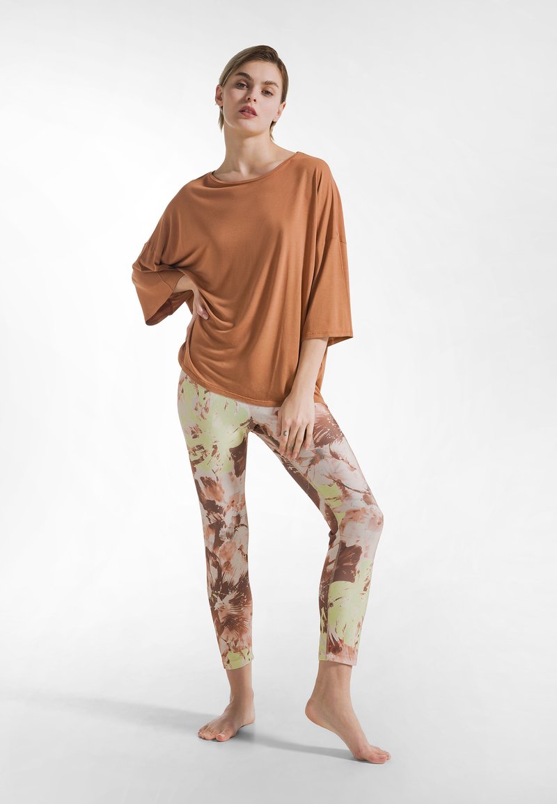 Camiseta marrón de gran tamaño con mangas anchas, combinada con leggings vibrantes de estampado floral en tonos verdes, rosas y marrones.
