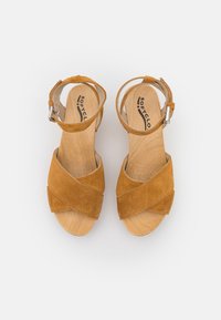 Tan suède sandalen met een kruisbandontwerp, verstelbare enkelriem en een natuurlijk houten zool. Gladde textuur met een minimalistische esthetiek.