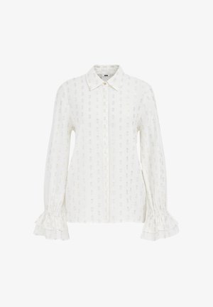 Valge pikade varrukatega pluus, millel on kraega kaelus, tekstuurne kude, peened metallilised mustrid ja volangidega mansetid.