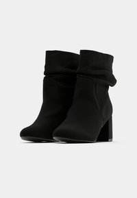 Μαύρα μποτάκια αστραγάλου με χαλαρή επάνω επιφάνεια, κατασκευασμένα από μαλακό ύφασμα. Σχεδίαση με τακούνι μπλοκ που προσφέρει σταθερότητα. Λείο υφή, μινιμαλιστικό στυλ.