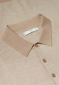 Polo en maille beige avec un col côtelé, trois boutons marron et une étiquette intérieure visible.
