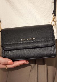 Black leather crossbody bag with a textured finish, gold branding on the front, flap closure, and a detachable strap.