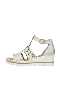 Wedge sandal in metallic silver, featuring cutout flower patterns, adjustable ankle strap, and a white rubber sole with scalloped edges.