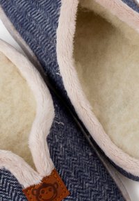 Granatowe kapcie z wzorem w jodełkę, beżowym, puszystym wykończeniem, różowym, pluszowym brzegiem i małą brązową metką z logo małpki.