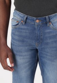 Světle modré džíny z denimu, s rovný střih, měděnými detaily, designem s pěti kapsami a jemným vyblednutím pro přidanou texturu.