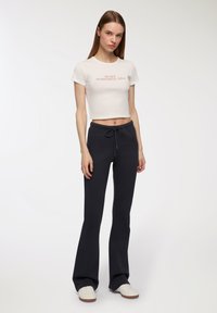 Biała krótka koszulka z napisem "W MOJEJ ERZE ROMANSU"; ciemnoszare dzwony dresowe z sznurkiem; noszona z białymi trampkami.