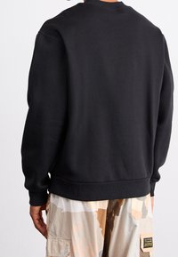 Black sweatshirt with a simple design, round neck, ribbed cuffs, and hem; soft texture. Back view shows no notable accents or patterns.