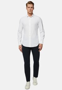 Chemise blanche à manches longues avec un col pointu, associée à un pantalon bleu marine et des baskets blanches. Matière en coton lisse, design ajusté.