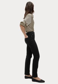 Jeans negros ajustados con cintura alta, combinados con una blusa a rayas en negro y crema. La modelo está de pie con una mano en el bolsillo, mirando hacia la izquierda.