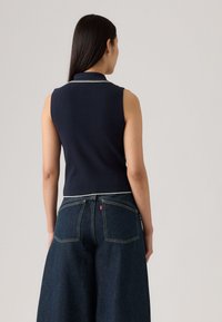 Top sans manches bleu marine avec une texture côtelée et un col blanc pipé, associé à un jean large taille haute bleu foncé.