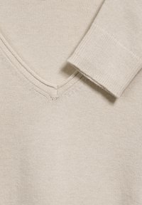 Beige stickad tröja med V-ringning och ribbade  ärmslut, som visar en jämn textur med subtila sömnadsdetaljer.